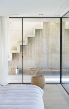 frameless sliding glass doors to a bedroom with white curtains and looking out on a stone staircase