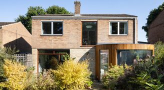 a rear, curved timber clad extension to a mid-century modern home with a frameless curved window