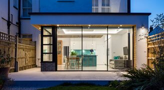 banner image of an extension in London using sliding glass doors with steel windows shown at night