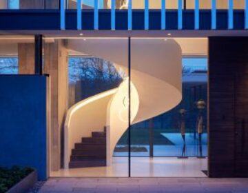 frameless sliding glass doors shown on the outside of a house at dusk looking into a stairwell
