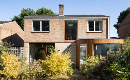 a rear, curved timber clad extension to a mid-century modern home with a frameless curved window