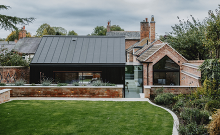 garden view of a modern extension to a traditional red brick gable end building with a glass link between