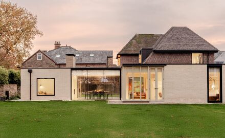 slim sliding glass doors and modern glazing to a house renovation and extension to a traditional cottage in york shown at dusk, viewing the house from the outside