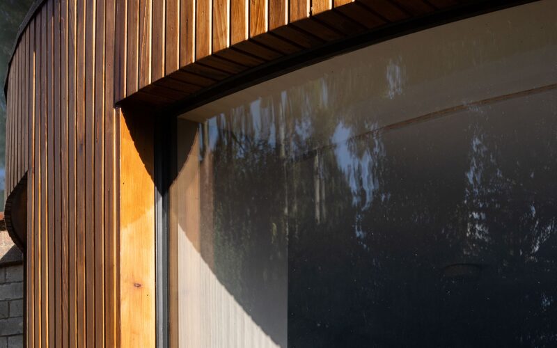 an up close detailed image of the connection between a curved frameless window with timber cladding