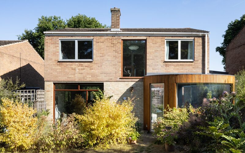 a rear, curved timber clad extension to a mid-century modern home with a frameless curved window