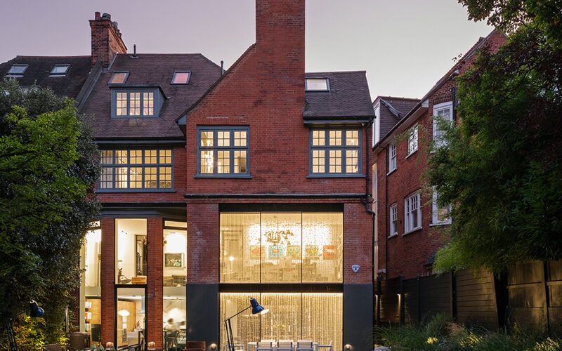 frameless windows to the rear of a brick London house shown at night with a manicured lawn