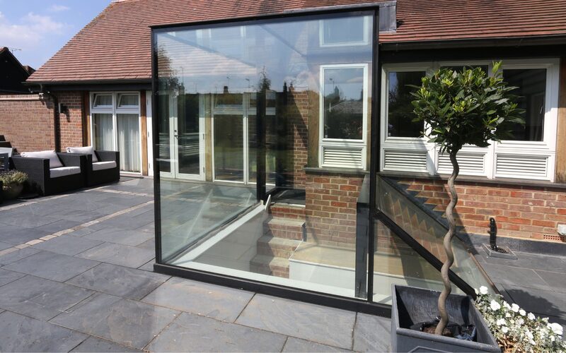 a glass box forming a shaped glass link to a basement sat on a grey patio