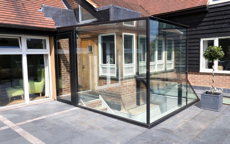 a glass box over a basement entrance on a patio attached to a traditional cottage house