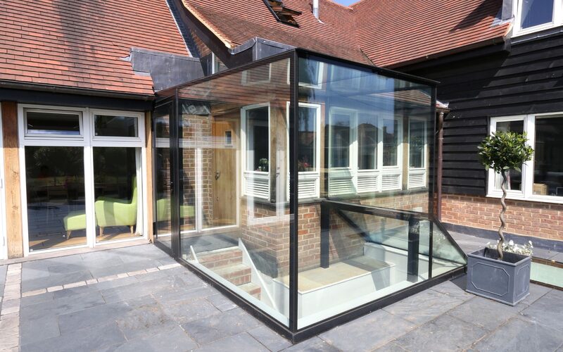 a glass box with a door within it sat over a staircase leading to a basement below a grey patio