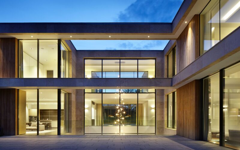 glass curtain walling across two storeys of a bespoke home, shown from the outside around a courtyard at dusk