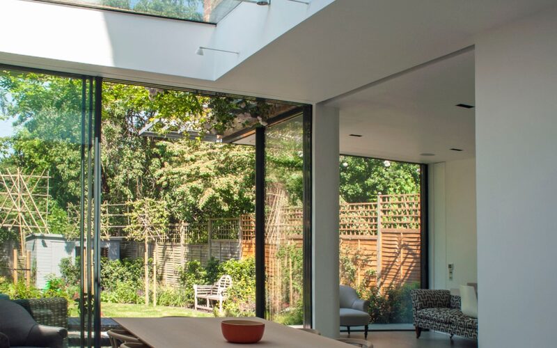 a glazed extension with a frameless rooflight with glass beams and slim framed sliding glass doors