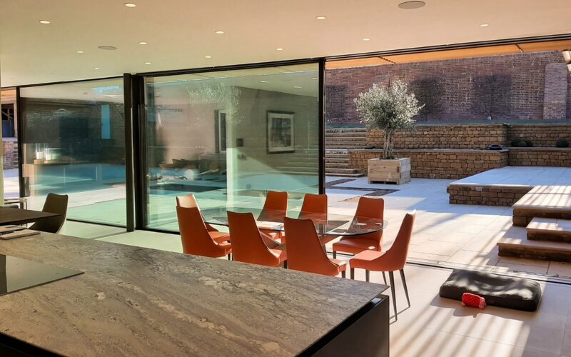 large glass doors to a passive house shown from the inside of a dining room looking out over a paved courtyard