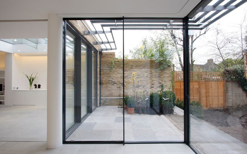 minimal sliding doors to a rear extension glass wall on a return shown from the inside overlooking patio