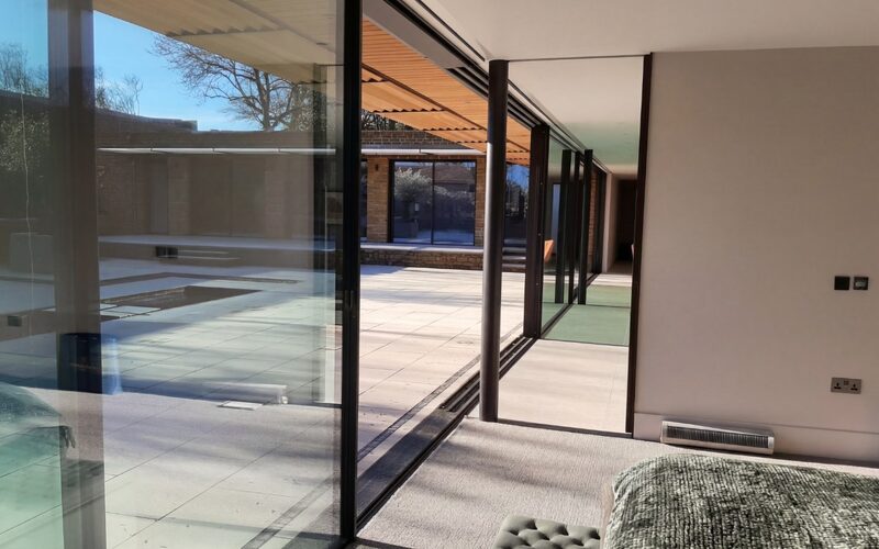 a sliding glass wall shown partially open to a passive house shown from the inside looking out over a paved courtyard.