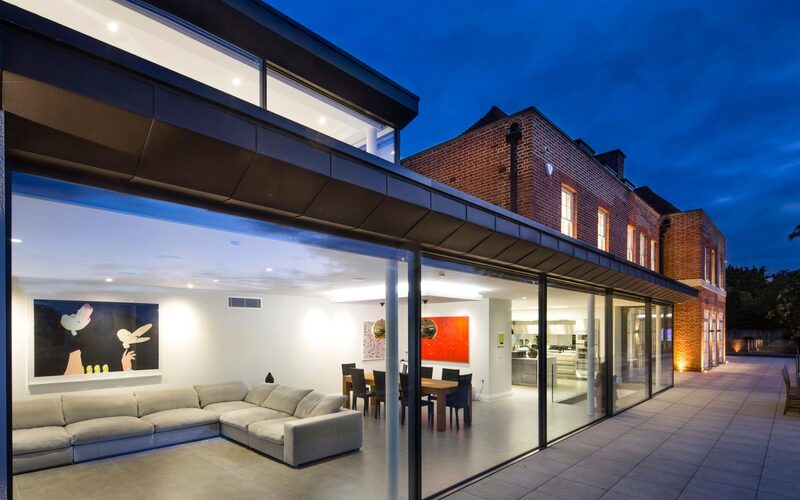 a long run of slim sliders to a glazed extension to a brick house in totteridge, shown at an angle and at dusk