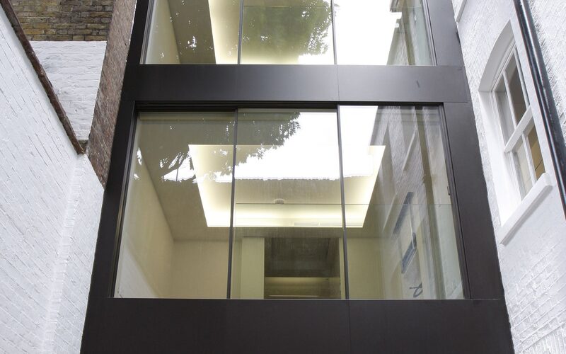 a three storey glass extension in London with sliding glass doors and metal cladding