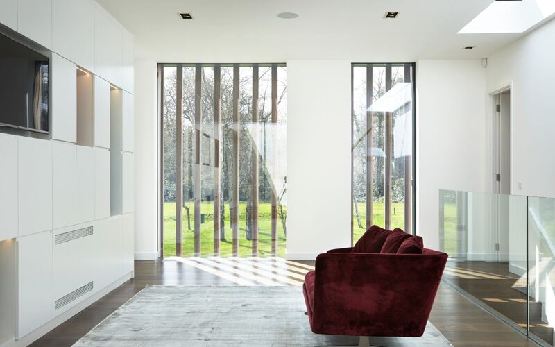 frameless windows shown from the inside of a white walled landing, looking out over lawn, showing fixed timber battens through the glazing