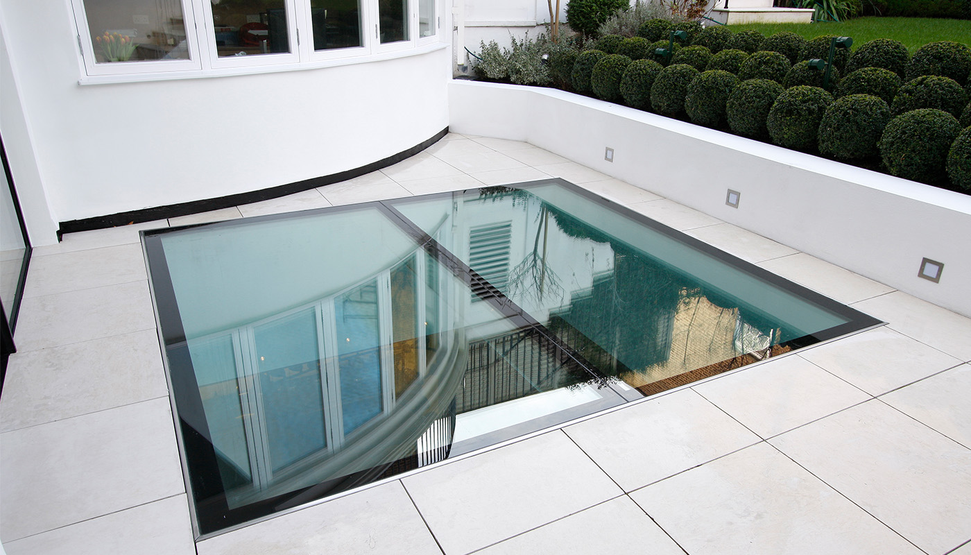 Frameless structural glass floor light above a basement wellness pool, an example of glazing for specialist wellness spaces.